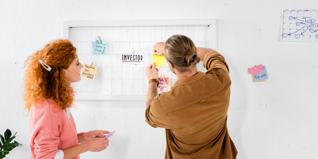 A man and woman sticking post-it notes to a brainstorming board